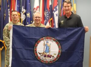 Virginia Governor Glenn Youngkin presents a Virginia flag to the command team for Joint Task Force Cardinal July 6, 2023, at Fort Barfoot, Virginia, prior to their departure for Texas where they will support border security operations.